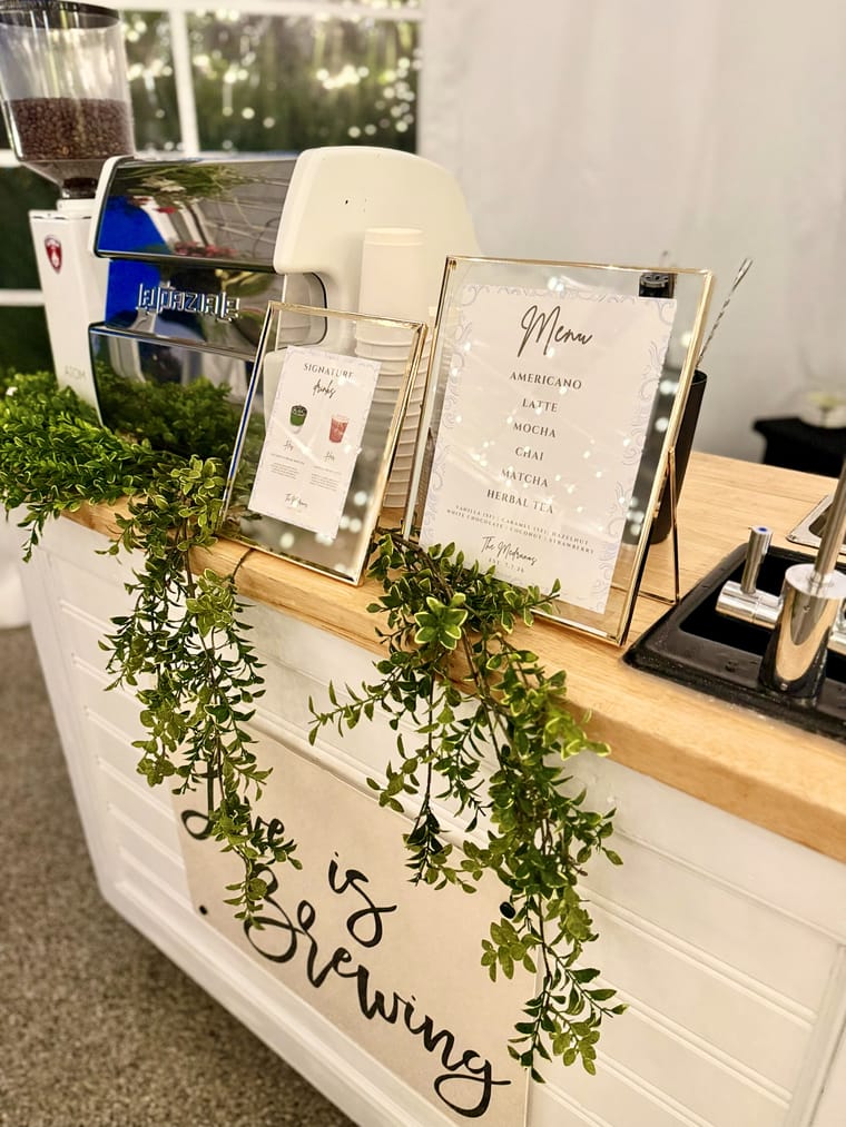 The coffee cart set up outdoors at a venue with greenery and framed menus.