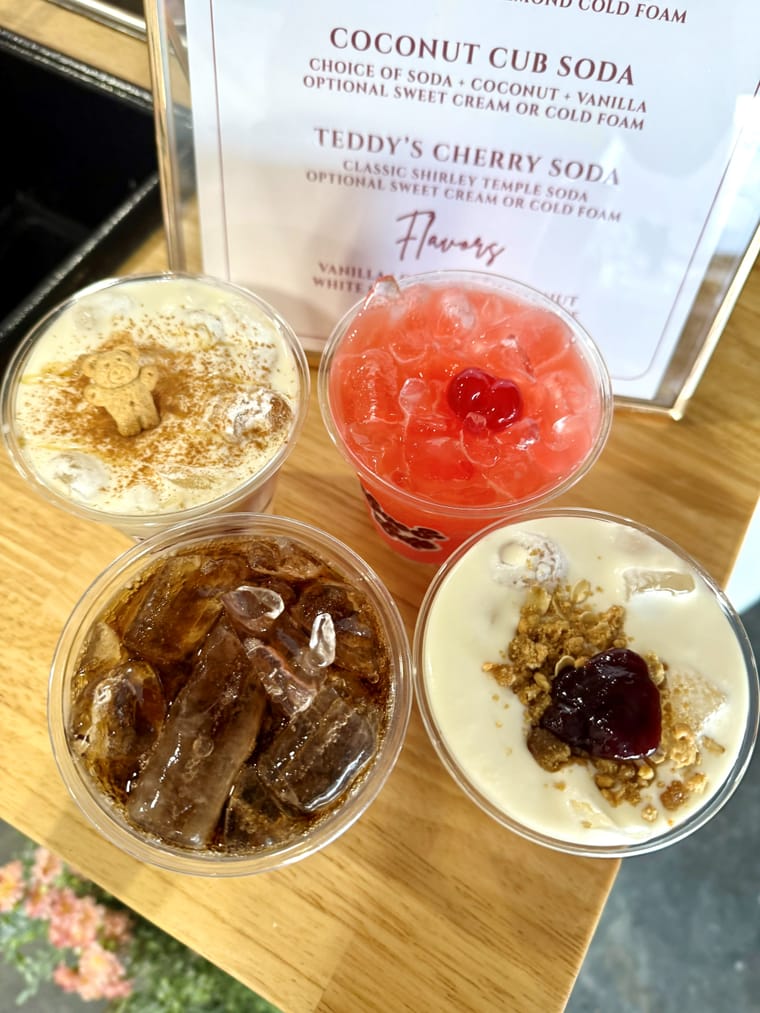 Four drinks including dirty sodas and iced lattes on a wooden board.