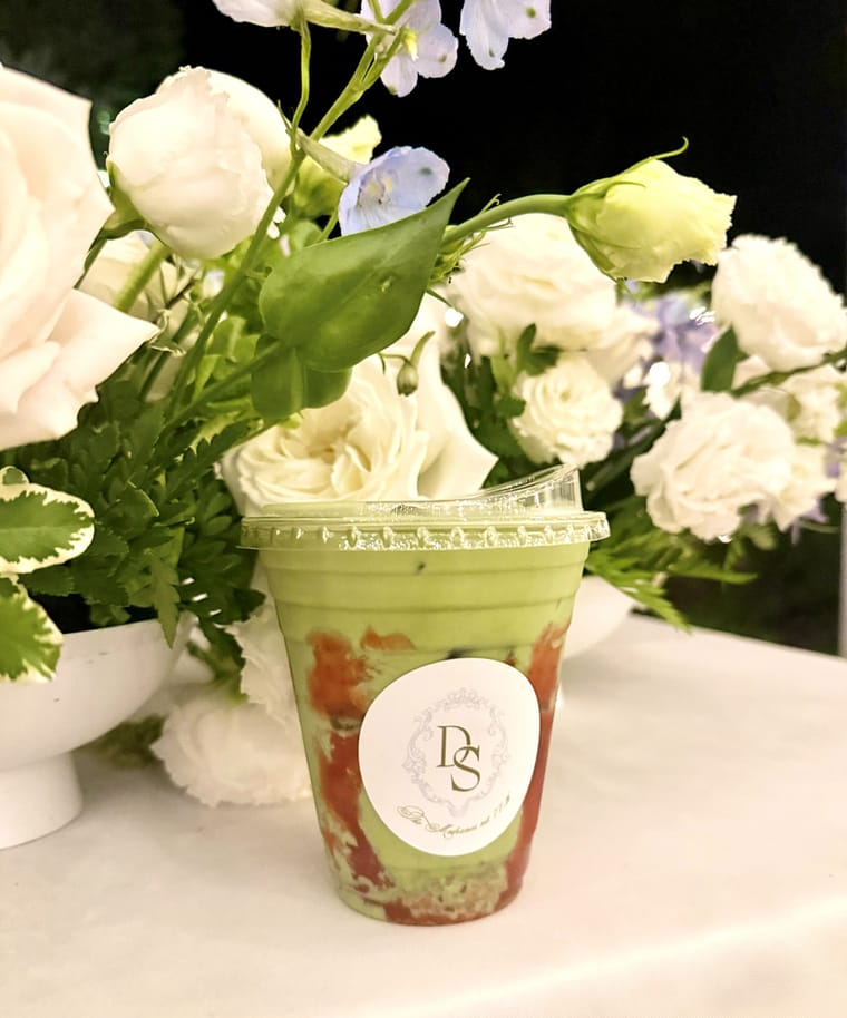 An iced matcha in a branded cup set among white roses.