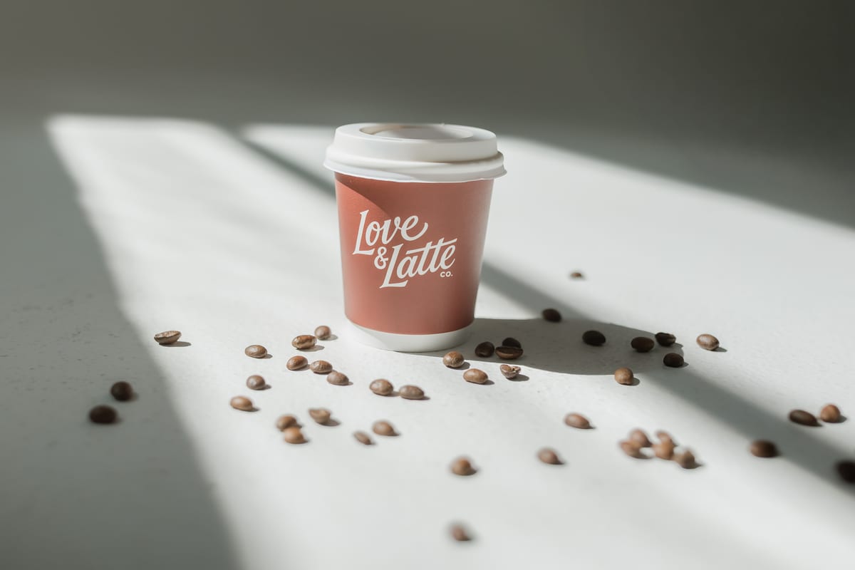 A branded Love and Latte cup in sunlight with coffee beans scattered around it
