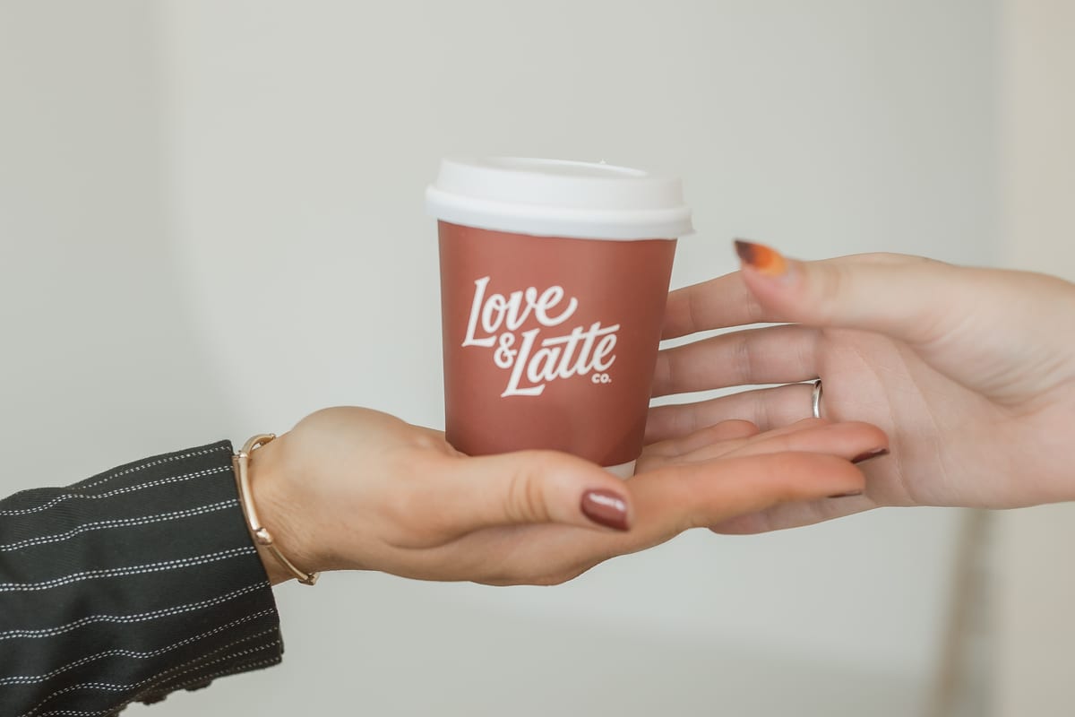 A branded Love and Latte cup held out on an open palm