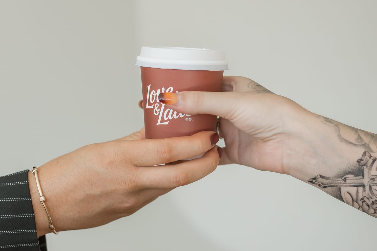 One hand passing a branded Love and Latte cup to another
