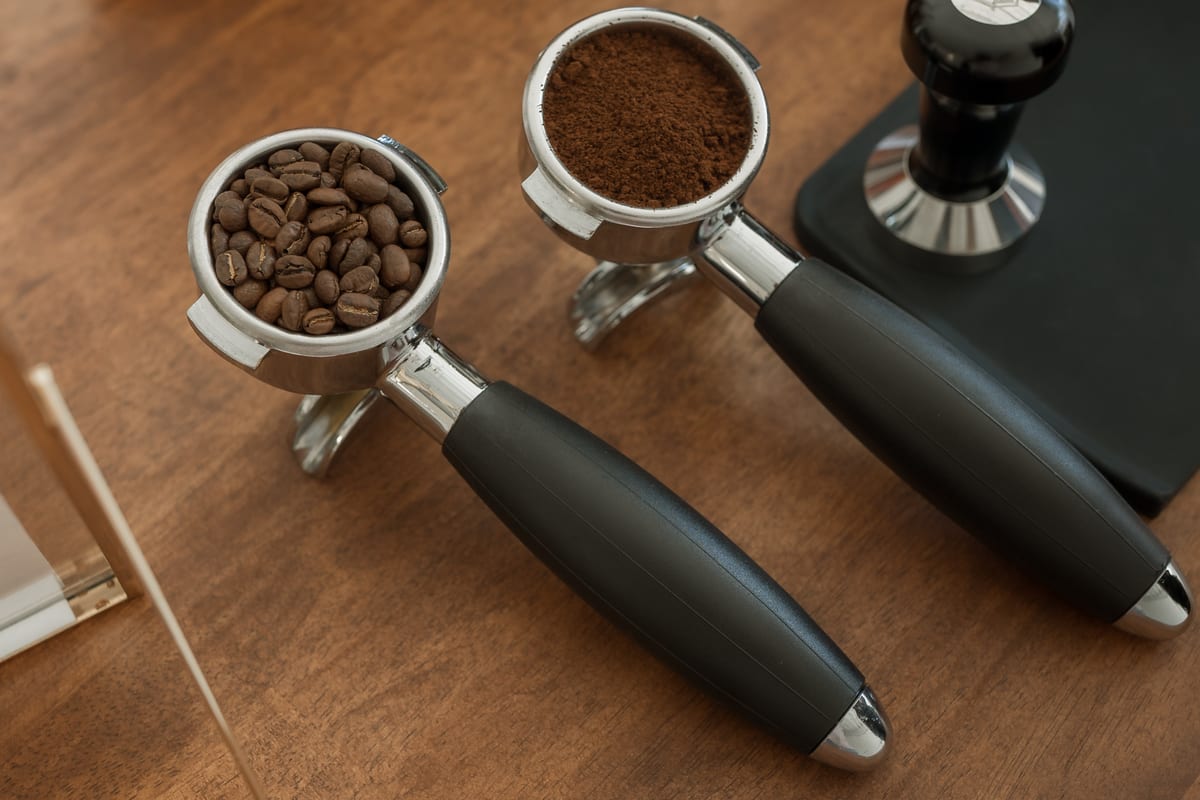 Two portafilters on the counter, one filled with beans and one with fresh grounds.