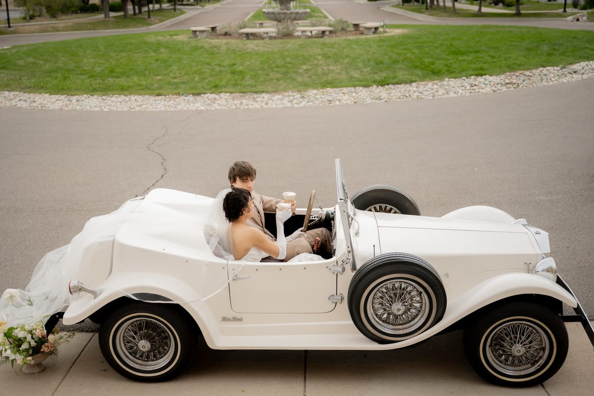 A white vintage car at a wedding with drinks from the cart.